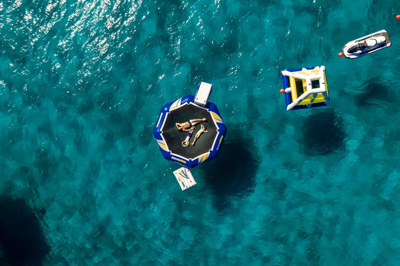Aerial view of people relaxing on a floating trampoline near CRN Starburst IV Yacht for Charter in clear blue water.