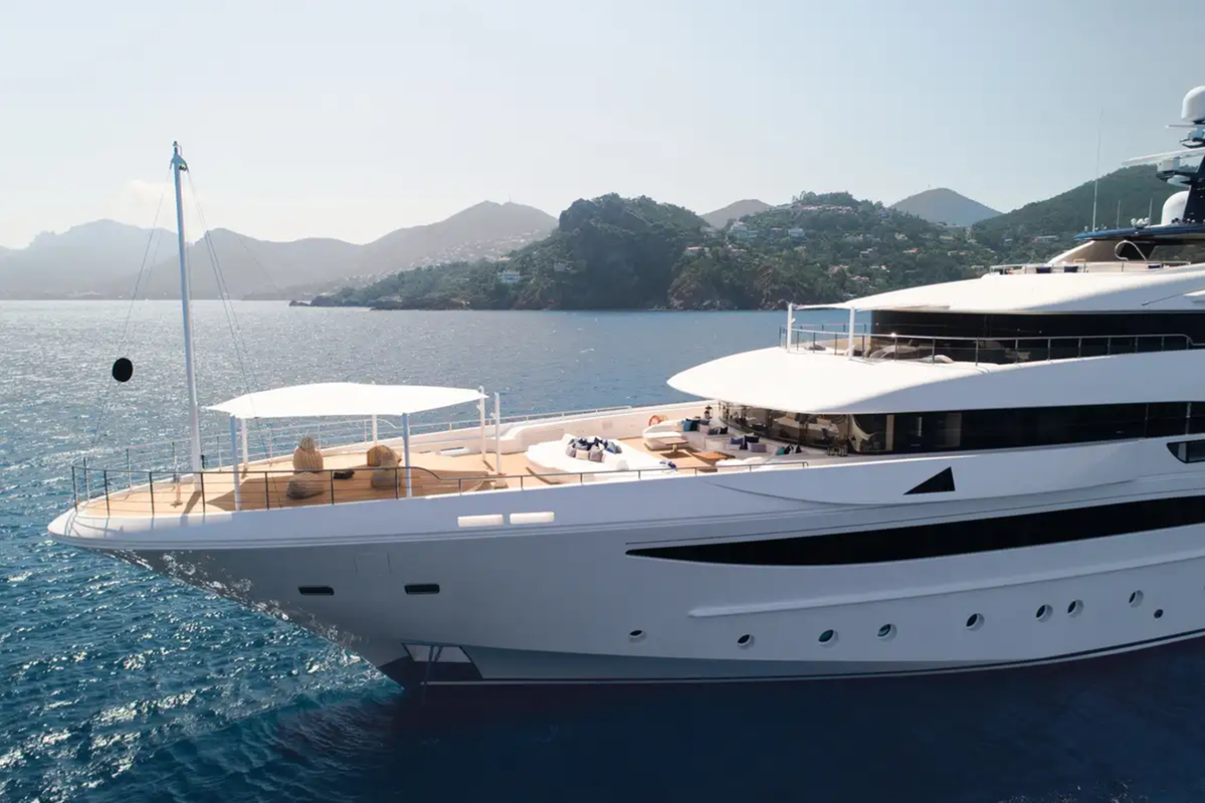The CRN Starburst IV Yacht for Charter floats on calm blue water with hills and greenery in the background under a clear sky.