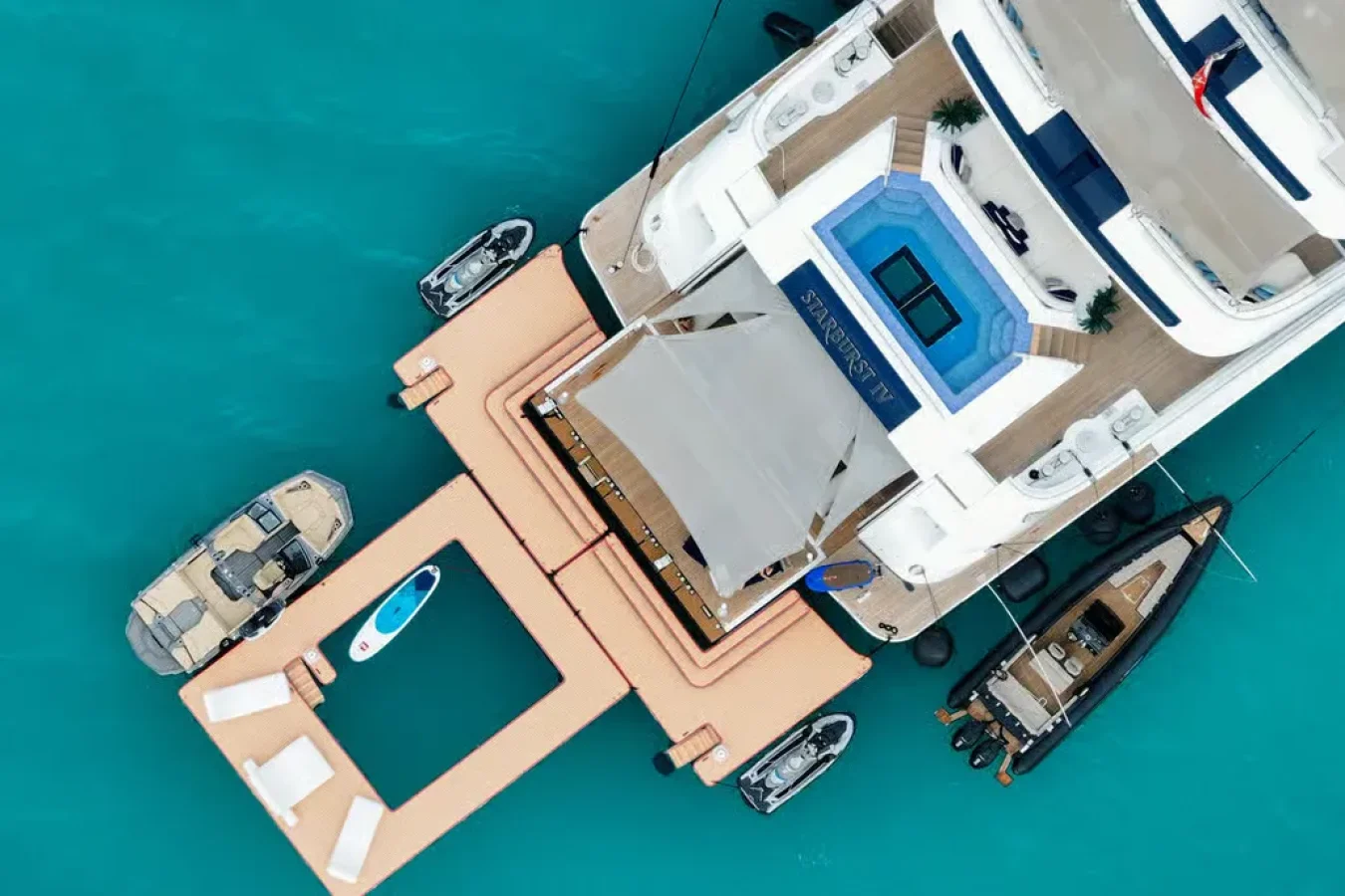 Aerial view of CRN Starburst IV Yacht For Charter with floating dock, pool, lounge chairs, boats, and paddleboard.