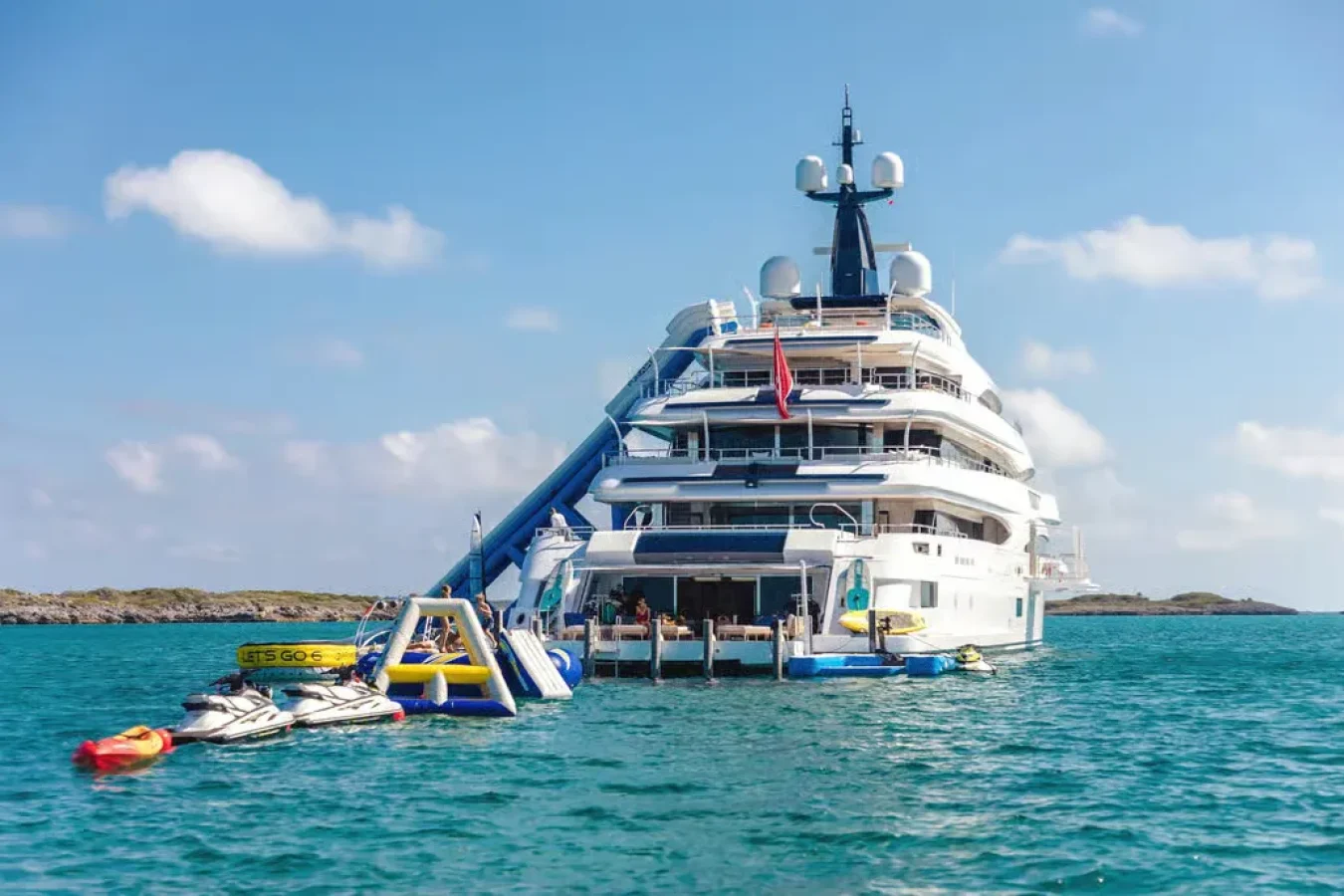 CRN Starburst IV Yacht For Charter: large white yacht with jet skis, inflatable slide, and water toys on blue water.